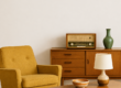 Een retro interieur met een mosterdgele fauteuil, houten dressoir met vintage radio, salontafel en tafellamp uit de jaren 50, 60 of 70